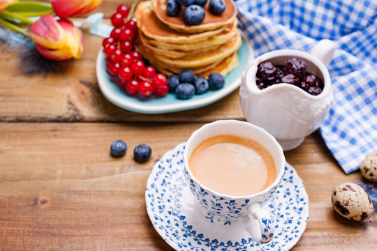 Pancakes with blueberries and currants for breakfast and fresh aromatic coffee. Spring breakfast with flowers on a wooden table. The concept of holidays and Easter.