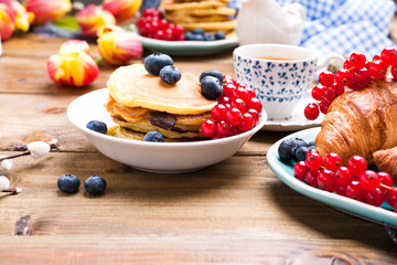 Pancakes with blueberries and currants for breakfast and fresh aromatic coffee. Spring breakfast with flowers on a wooden table. The concept of holidays and Easter.