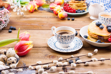 Fresh morning coffee and pastries homemade for breakfast. Pancakes with berries for a romantic breakfast and spring flowers. The concept for Easter and home comfort.