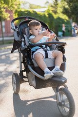 Obraz premium handsome boy sits in a stroller and drinks water from a bottle on a hot summer day