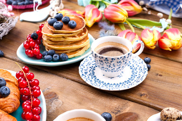 Fresh aromatic coffee in a vintage cup, homemade pastries for breakfast with blueberries and currants, on a wooden background and spring tulips. Free space for text.