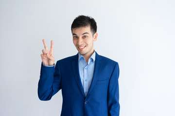 Smiling young business man showing victory sign. Guy looking at camera and celebrating success. Victory concept. Isolated front view on white background.