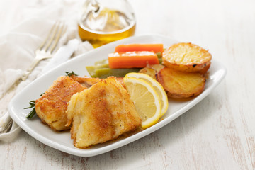 fried cod fish with lemon and vegetables on white plate