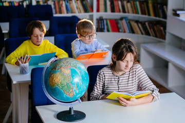 Three children reading open books, bright colorful covers. School kids different age studying sitting in class room. Education, elementary school, learning and people concept.