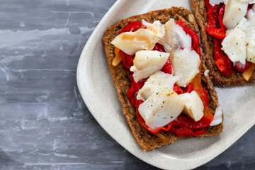 black healthy bread with cod fish and red pepper on dish
