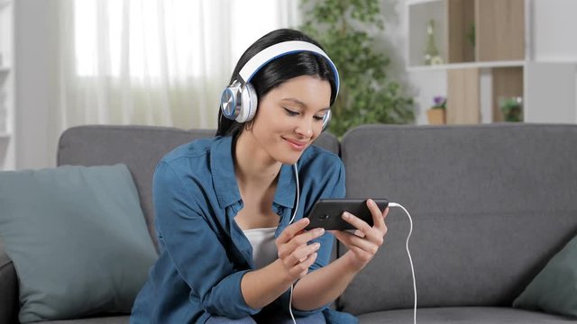 Relaxed woman watching videos on smart phone sitting on a couch at home