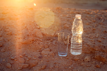 Glass and bottle of water on sand in the desert. Thirsty and drought concept