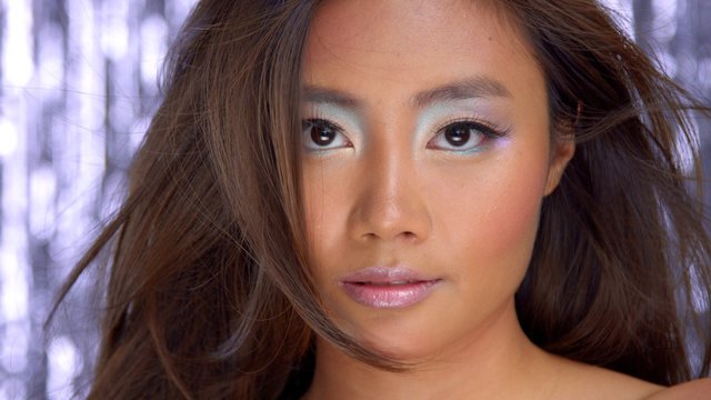 thai asian model in studio with silver rain disco background and party makeup looking straight to the camera