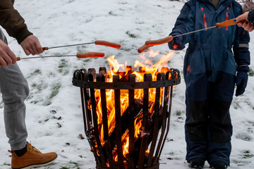 Closeup of family at a campfire grilling hot dog food. Winter snow outdoor scene.