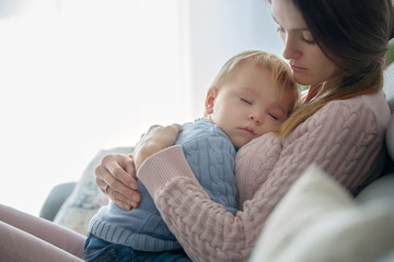 Young mother, holding her sick toddler boy, hugging him at home