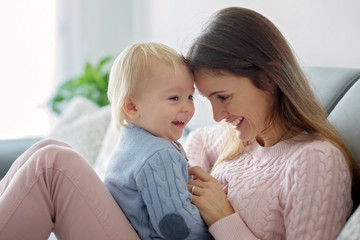 Young mother, holding her sick toddler boy, hugging him at home