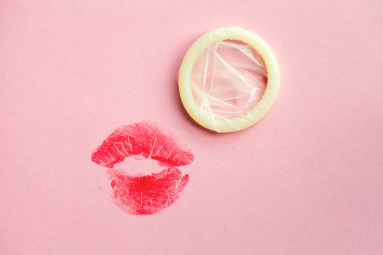 white condom and red lipstick kiss on pink background, safe sex concept, love affair