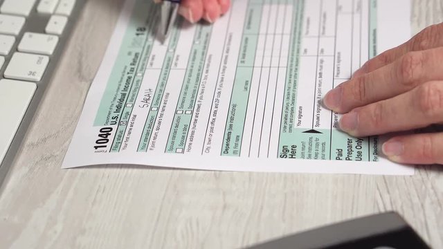 Closeup video of woman filling tax form 1040 aon the desk next to computer keyboard and calculator. 4k video