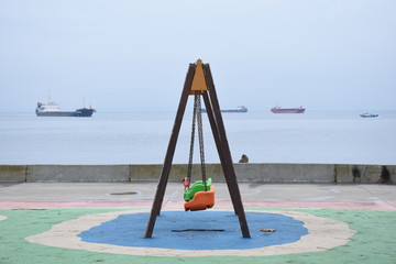 Fototapeta premium swing in thean empty swing on the shore, sea and ships in the background