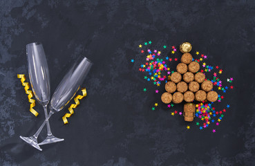 two empty glasses and Christmas tree made from used champagne bottle corks with colorful confetti   on black background with copy space