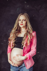 Pregnant woman in jeans holds hands on belly on a black background. Pregnancy, maternity, preparation and expectation concept. Close up, copy space, indoors. Beautiful tender mood photo of pregnancy