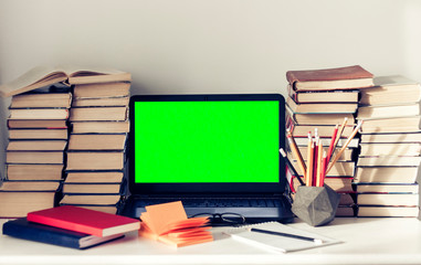Green screen laptop, stack of books, notebooks and pencils on white table, education office concept background.