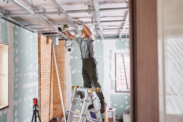 Room repair. Interior finish. young builder makes a plasterboard ceiling, standing on a stepladder