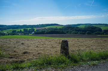 Blick auf einen Grenzstein in Oberbayern mit den Gatterbergen im Hintergrund und einem sommerlich blauen Himmel mit wenigen weißen Wolken