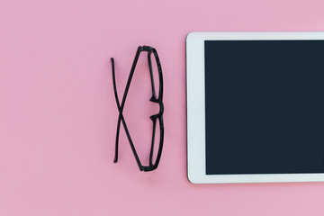 White tablet computer with reading glasses on pink color background minimal office