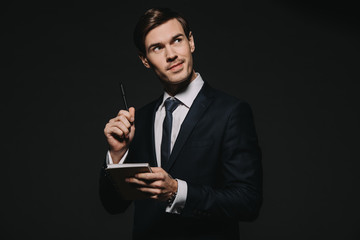persive businessman holding notebook and pen in hands isolated on black