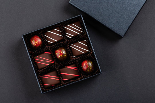 Assortment of luxury bonbons with red splashes in box on black background