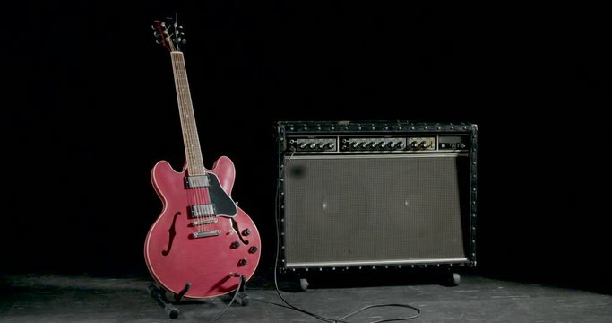 Hand puts electric guitar on a stand next to a guitar amp
