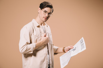 handsome man looking at camera while holding travel newspaper isolated on beige
