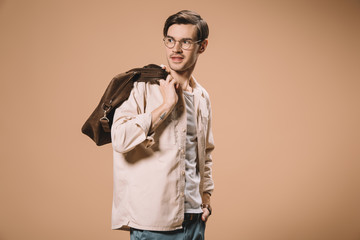 handsome man standing with hand in pocket and holding bag isolated on beige