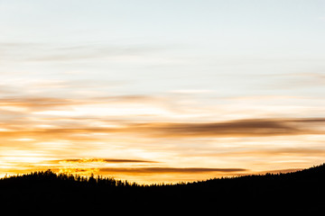 Golden stratus clouds above mountain silhouette. Sunset in mountain valley