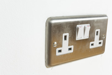 Stainless steel UK plug socket on white wall