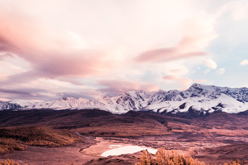 Pink and purple clouds over mountain range. Sunset or dawn in mountains in autumn. Hiking trip to valley of mountains.