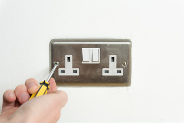 Screwdriver and Stainless steel UK plug socket on white wall