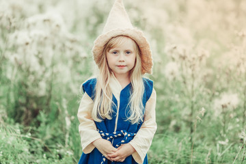 Close up portrait of cheerful blondie little caucasian girl in field in blossom in gnome's hat