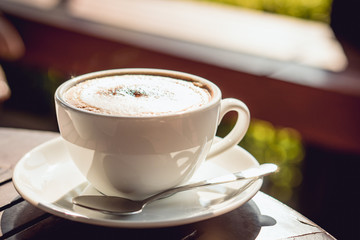 Hot coffee place on the wooden table in early morning, white cup and silver spoon.