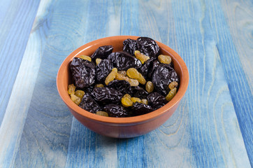 Dried plum and grapes in a bowl on a blue natural background top view