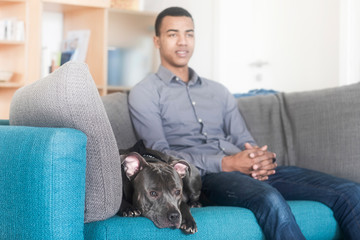 Junger Mann mit Hund zu Hause auf einem Sofa sitzend
