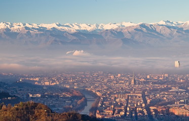 Obraz premium Panoramic view at sunrise on Turin city seen from Superga in winter, with a layer of smog that falls on buildings, snowy Alps mountains on background