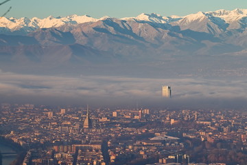Naklejka premium Panoramic view at sunrise on Turin city seen from Superga in winter, with a layer of smog that falls on buildings, snowy Alps mountains on background