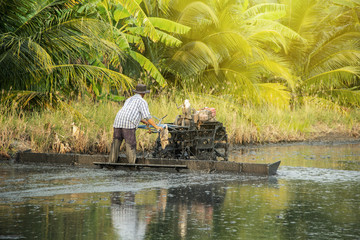Farmer using tiller tractor plowing in rice field. landscape surrounding area is filled with...