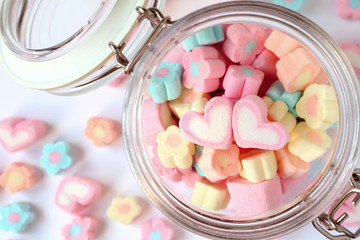 A Pair of Pink Heart on the Pile of Pastel Flower Shaped Marshmallow Candies in a Glass Jar with Some Scattered on the Table 