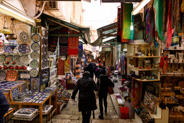 Naklejka premium Niektórzy ludzie spacerują ulicami starego miasta Jerozolimy ze straganami i sklepami z pamiątkami i jedzeniem.