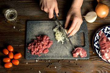 female hands cut onions, meat is near