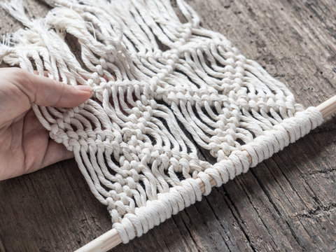 Macrame. Girl weaves macrame. White thread, female hand, wooden background, closeup
