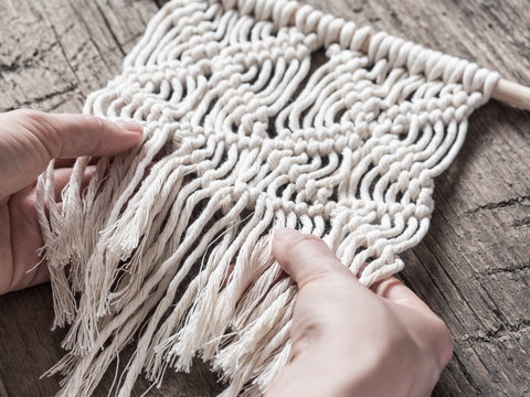 Macrame. Girl weaves macrame. White thread, female hand, wooden background, closeup