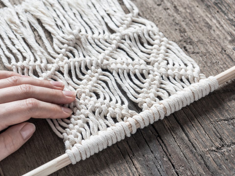 Macrame. Girl weaves macrame. White thread, female hand, wooden background, closeup