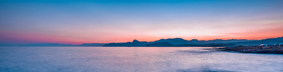 Beautiful mysterious marine landscape at sunset. Mountains, volcanic reef and ocean, panoramic banner.