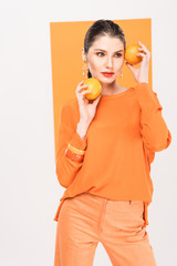 beautiful stylish woman holding oranges, looking away and posing with turmeric on background