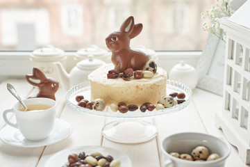 Rustic Easter Cake with Chocolate bunnies and Eggs. Easter greeting card background, closeup with copy space. Easter sweets for children. Chocolate bunny on decorated cake stand for Easter brunch.