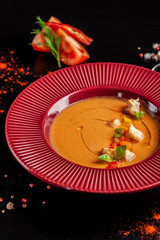 Concept of Spanish cuisine. Tomato soup Gazpacho from fresh tomatoes. Beautiful serving dishes in a red plate on a black table in a restaurant. background image. copy space